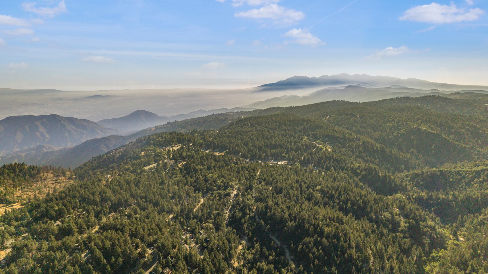 Aerial looking out across forested ridgelines toward the horizon.